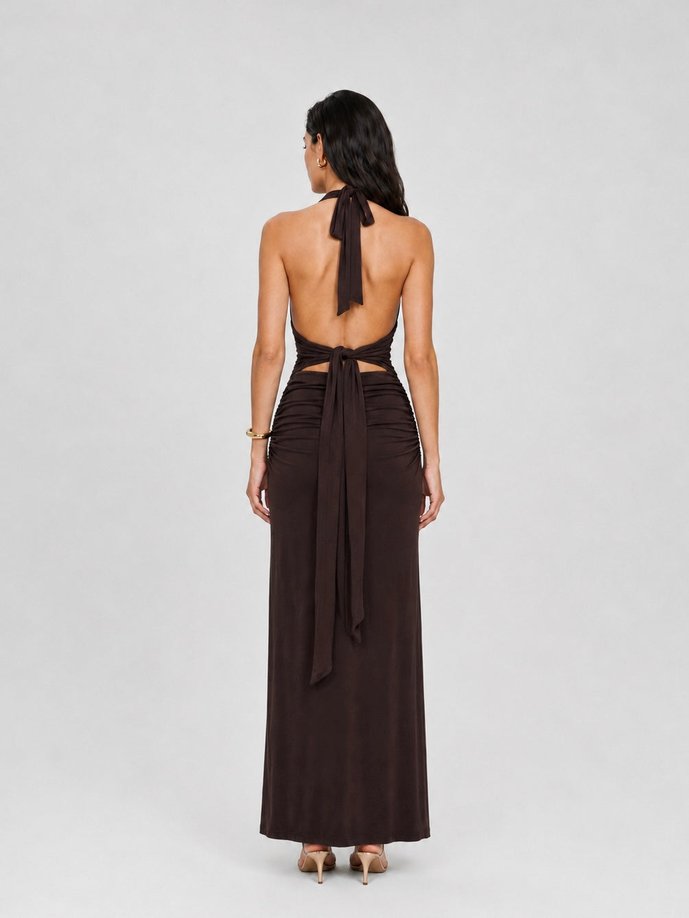 A woman viewed from the back wearing the Elévaison Vivienne coffee deep V-neck halter maxi dress with a ruched waist, against a light gray studio background.