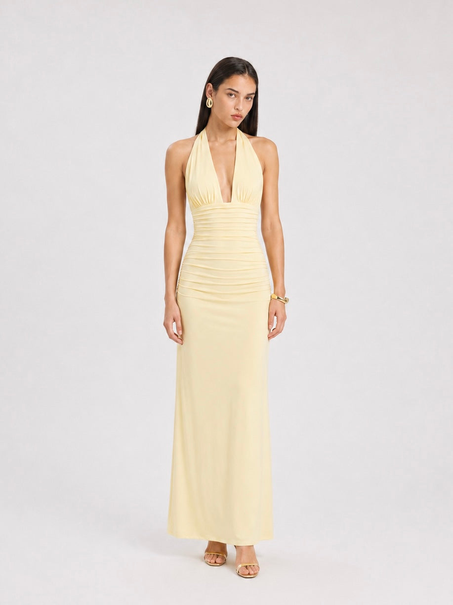 A woman wearing the Elévaison Vivienne light yellow deep V-neck halter maxi dress with a ruched waist, viewed from the front, against a light gray studio background.