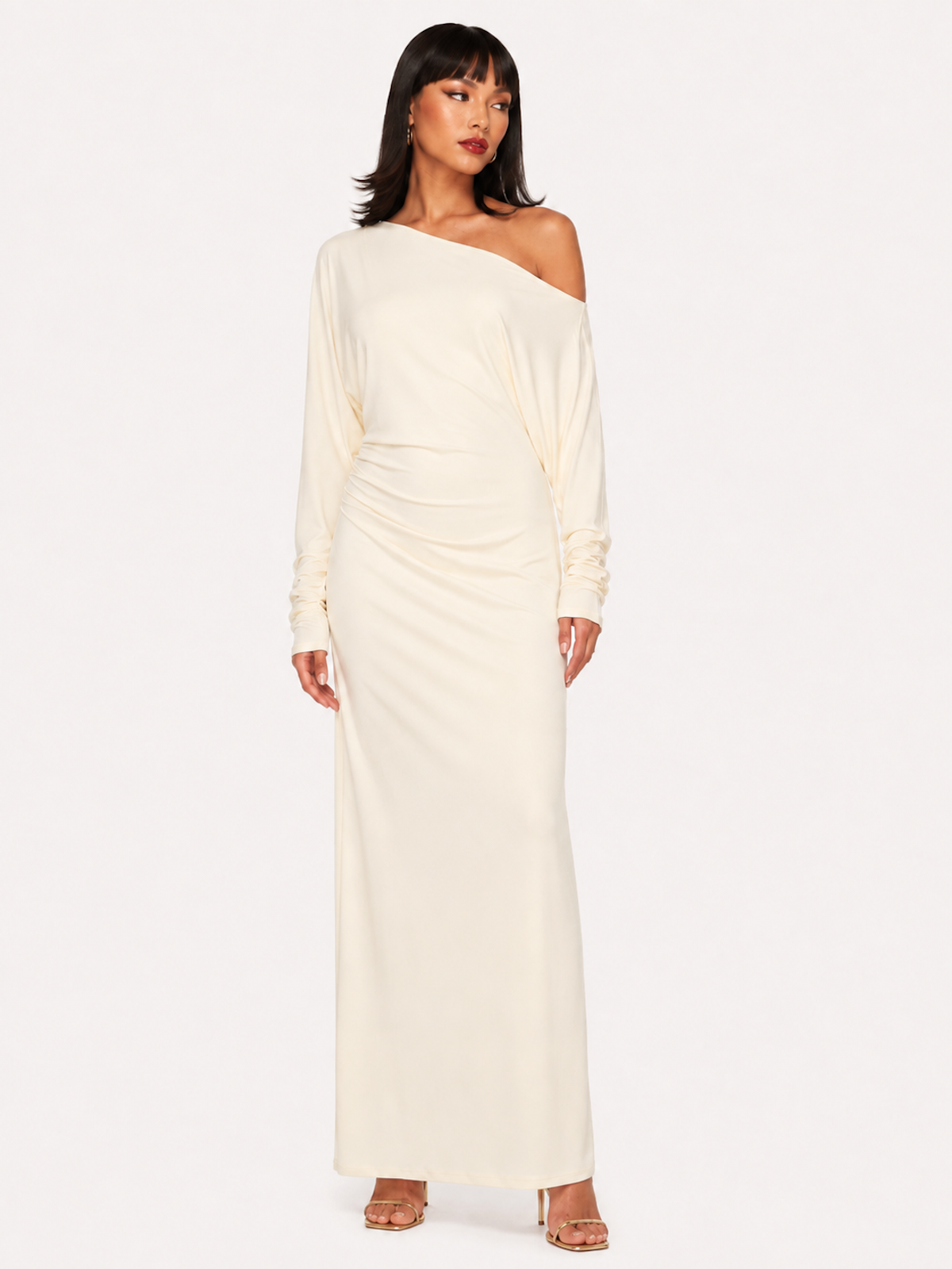 A woman wearing the Elévaison Arielle white asymmetric off-shoulder maxi dress, viewed from the front, against an ivory studio background.