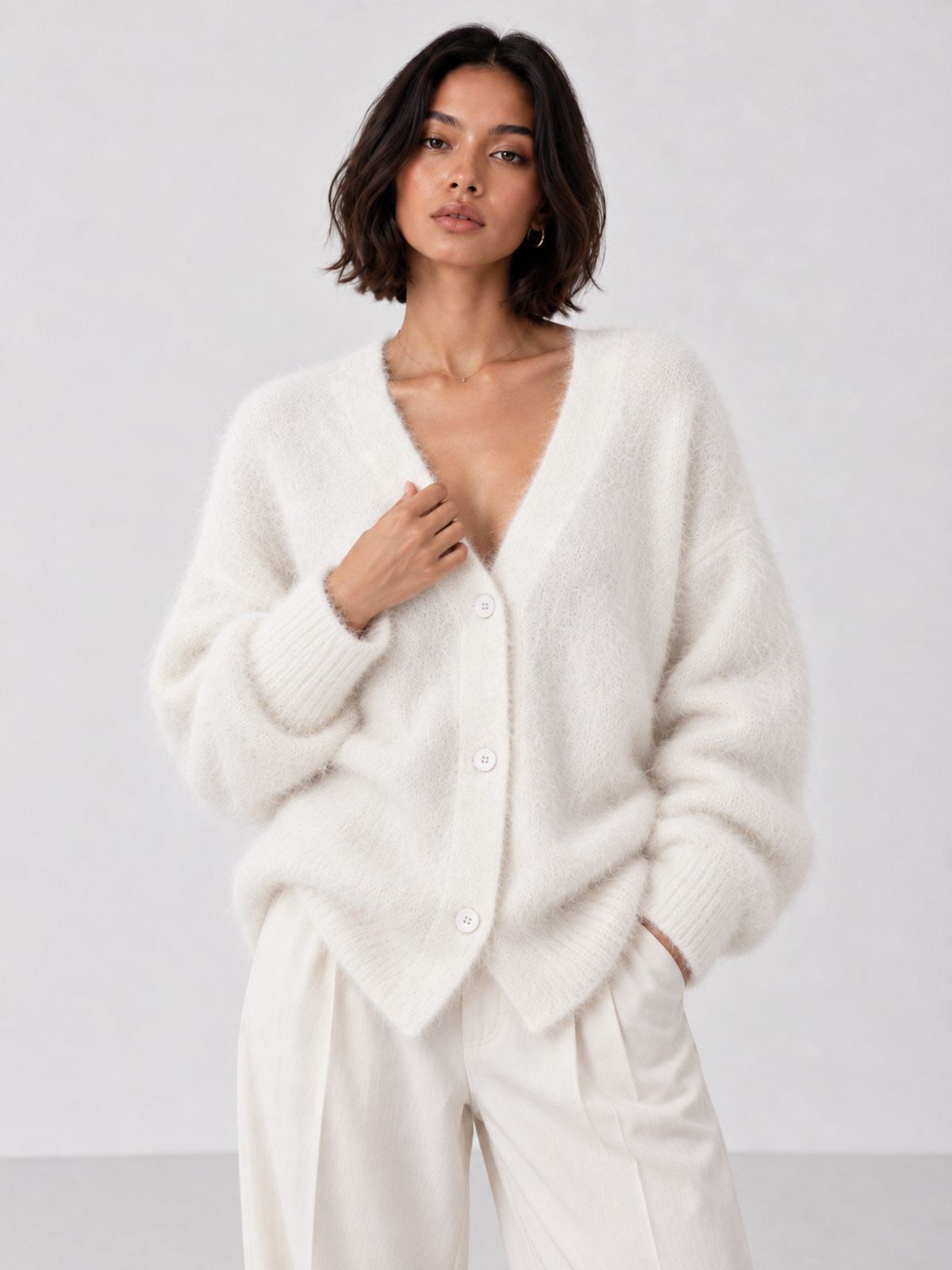 Front view of the white Elévaison Alina Cardigan with a V-neck, button front and ribbed cuffs against a light gray seamless backdrop.