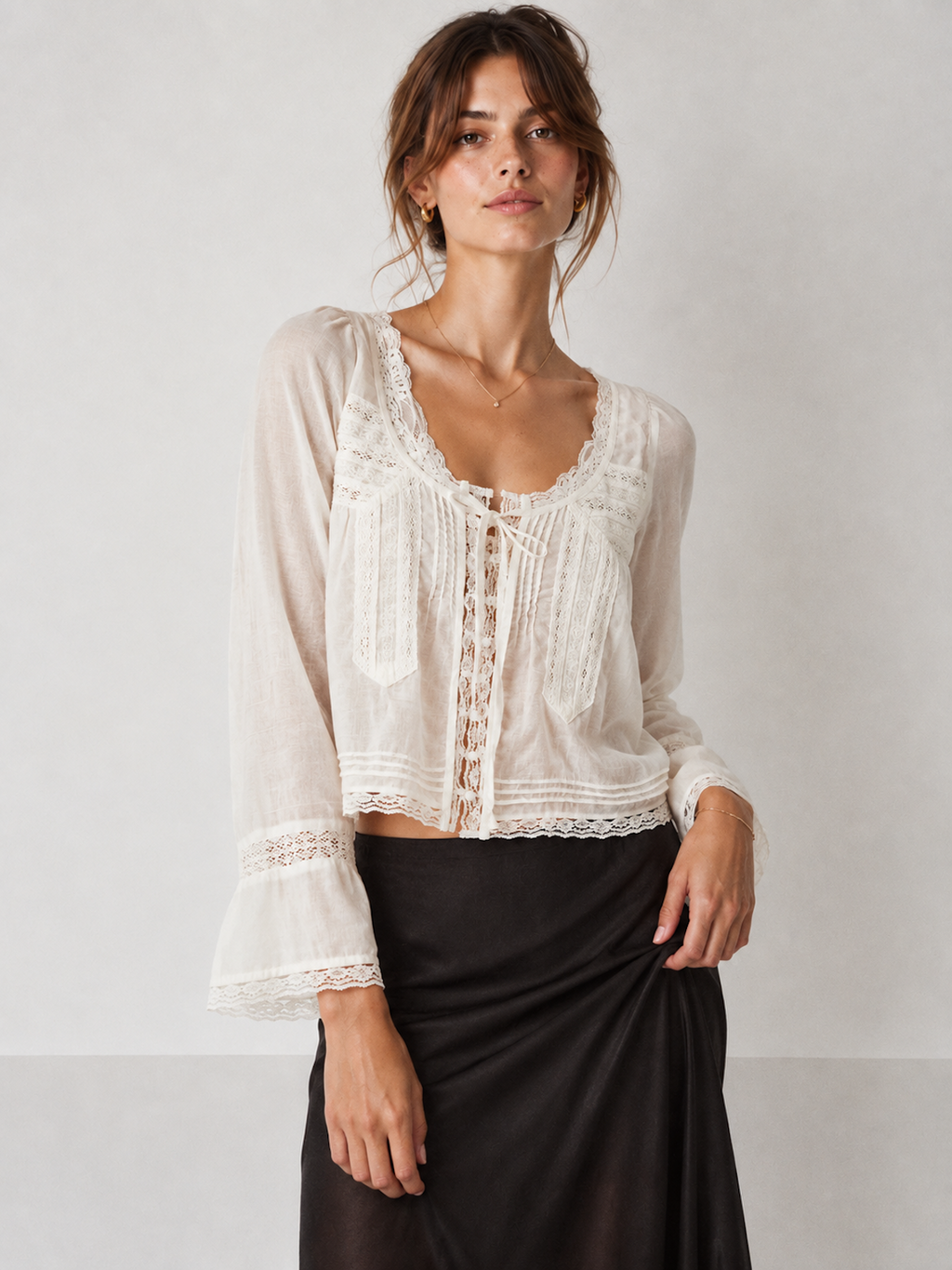 Model wearing the White Elévaison Celine Blouse with a scalloped lace neckline and tie-front detail in a pale gray studio.