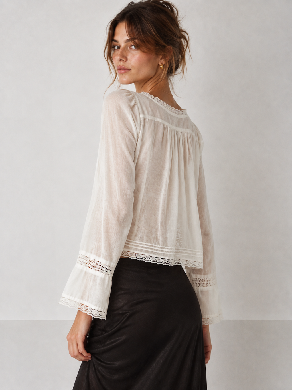 Back view of the White Elévaison Celine Blouse, showing the gathered back yoke and lace-trim cuffs in a pale gray studio.