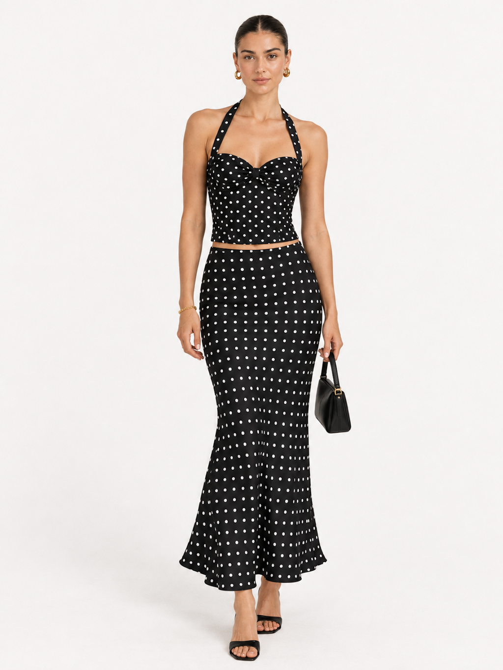 Model wearing the Midnight Polka Elévaison Thalia Two Piece with a halter top and flared midi skirt in a pale gray studio.