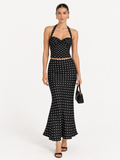 Model wearing the Midnight Polka Elévaison Thalia Two Piece with a halter top and flared midi skirt in a pale gray studio.