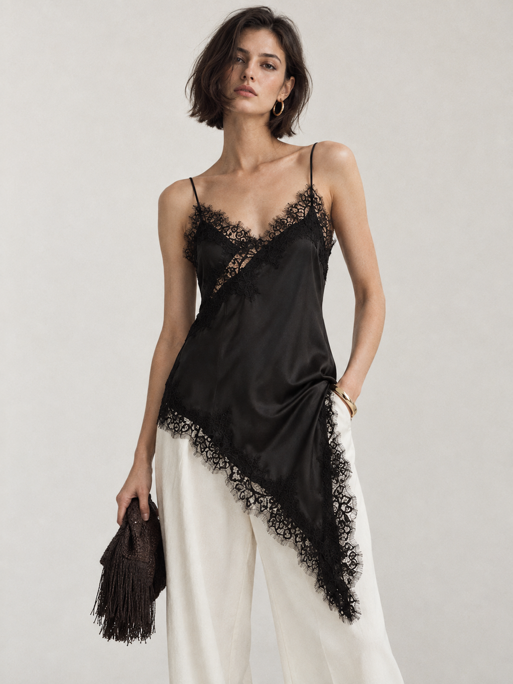 Model wearing the Black Elévaison Renata Sleeveless Top with lace trim and an asymmetric pointed hem in a pale gray studio.