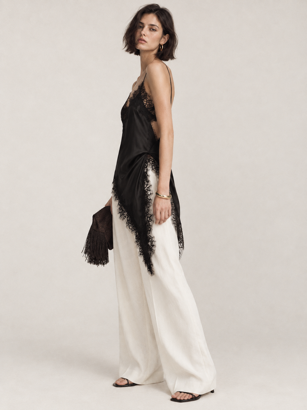 Side view of the Black Elévaison Renata Sleeveless Top with lace trim and a pointed asymmetric hem in studio.