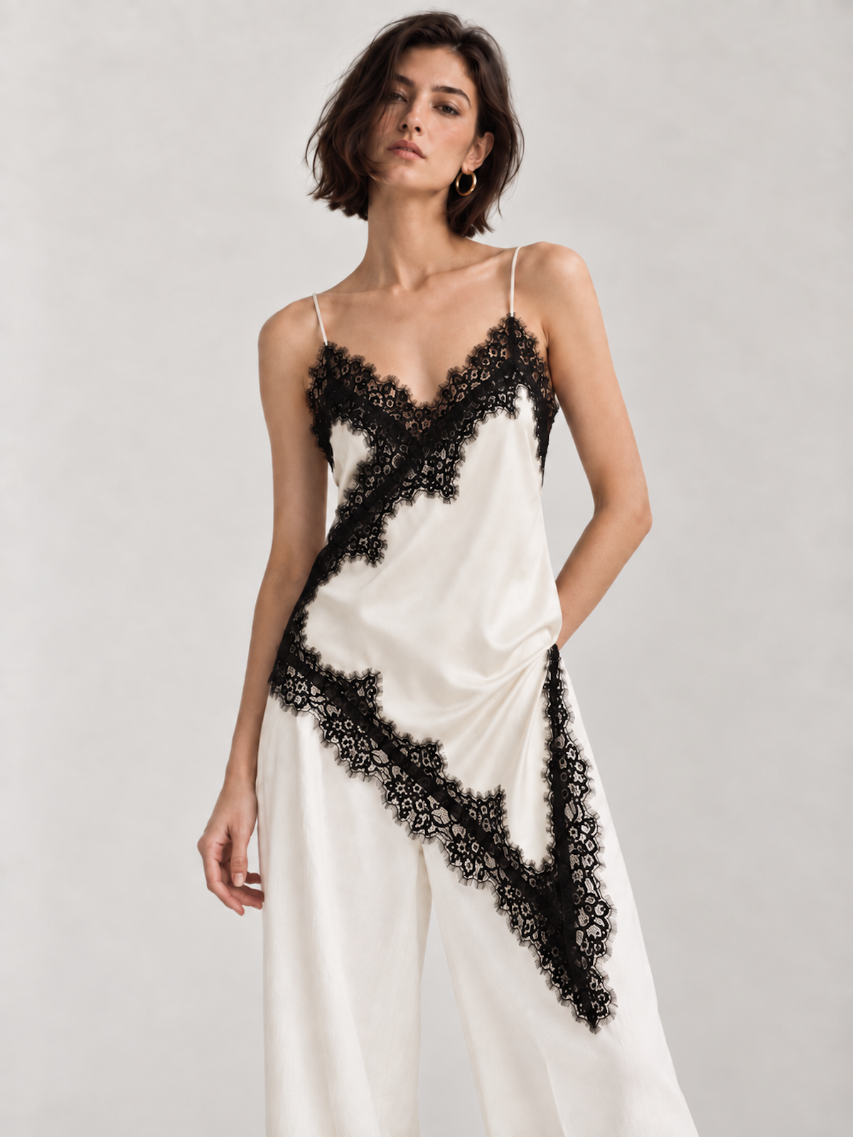 Front view of the ivory Elévaison Renata Sleeveless Top with black lace trim and a pointed asymmetric hem against a light gray seamless backdrop.