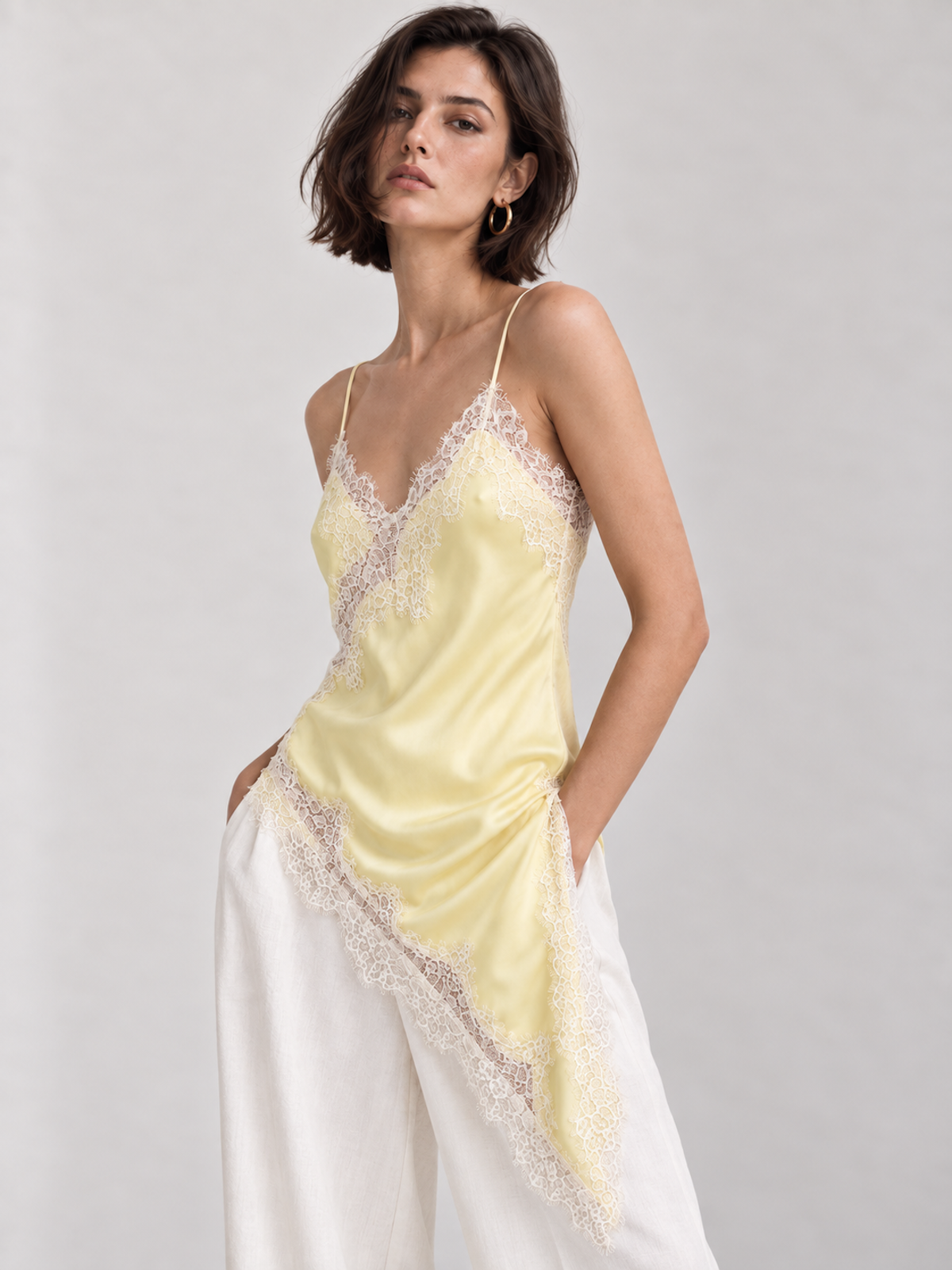 Front view of the pale yellow Elévaison Renata Sleeveless Top with contrast lace trim and a pointed asymmetric hem against a light gray seamless backdrop.