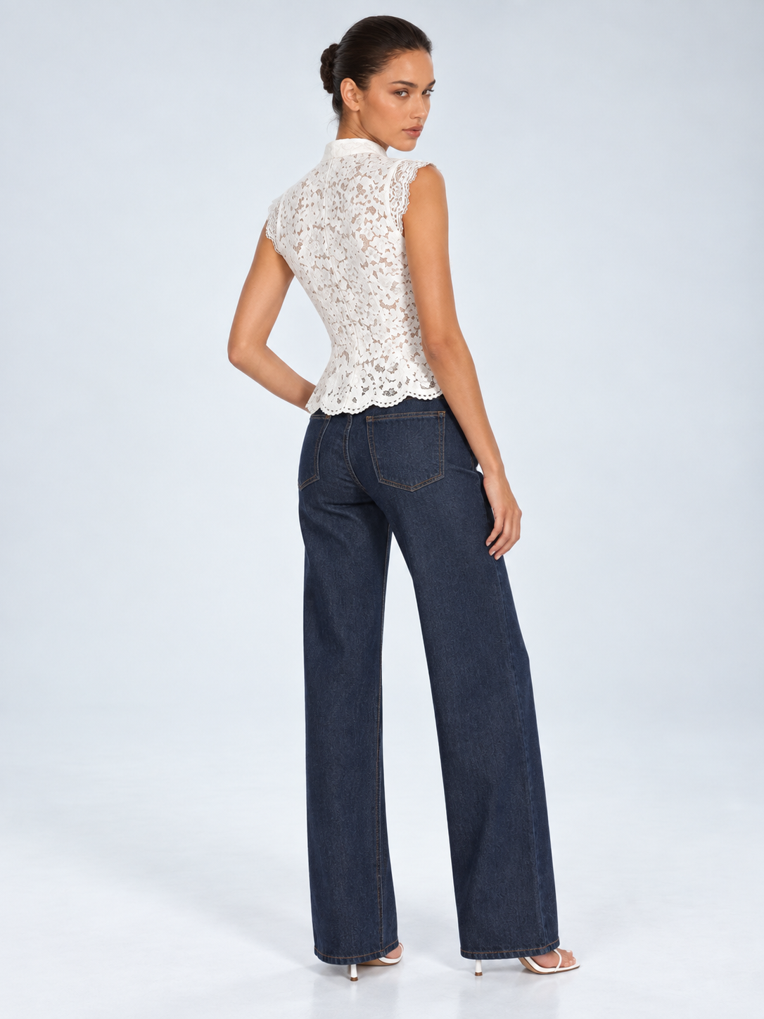Elévaison Isadora Blouse in white, back view showing a stand collar and scalloped lace hem, styled with dark wide-leg jeans against a pale blue studio background.