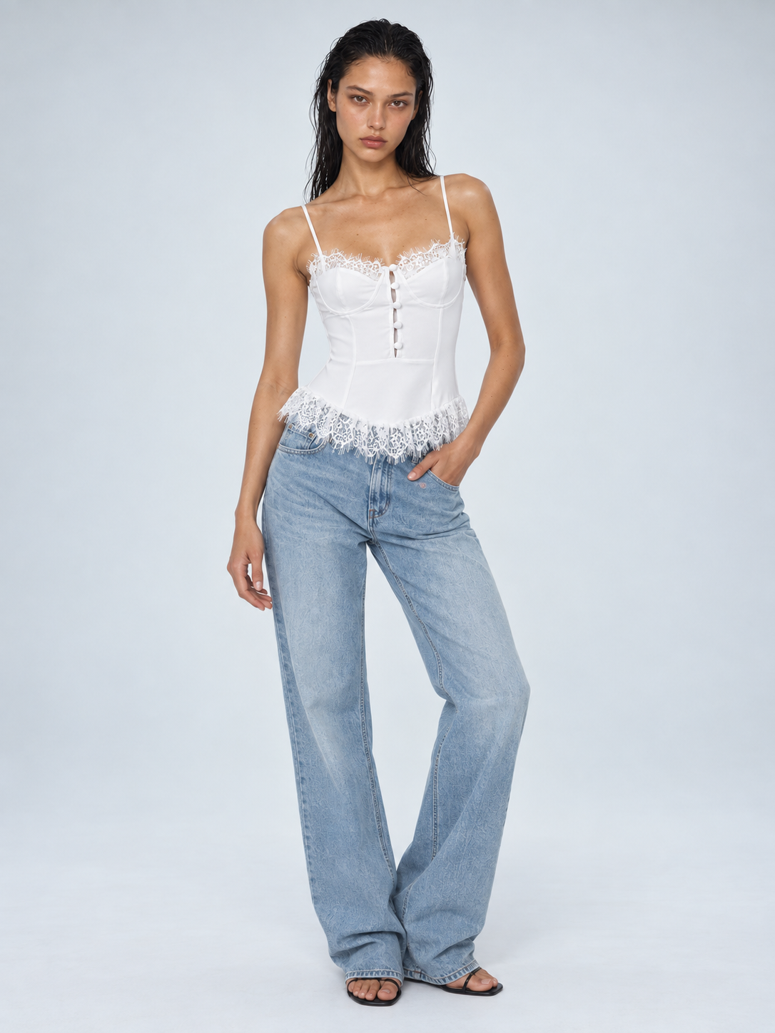 Elévaison Belle Tank Top in white, front view showing a fitted corset bodice, button detail and lace trim, styled with light blue jeans against a pale blue studio background.
