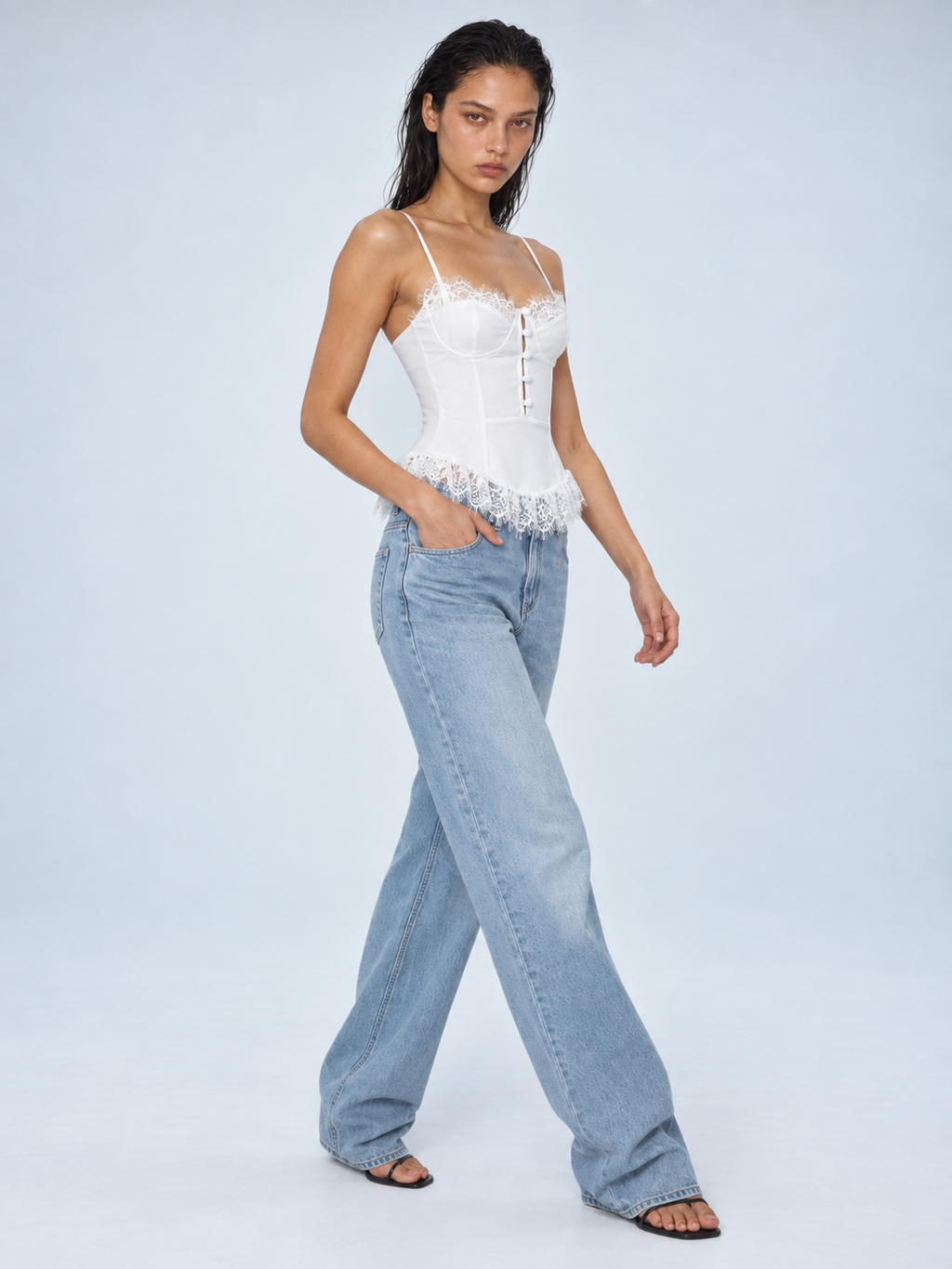 Elévaison Belle Tank Top in white, three-quarter view showing a fitted corset bodice, thin straps and lace trim, styled with light blue jeans against a pale blue studio background.
