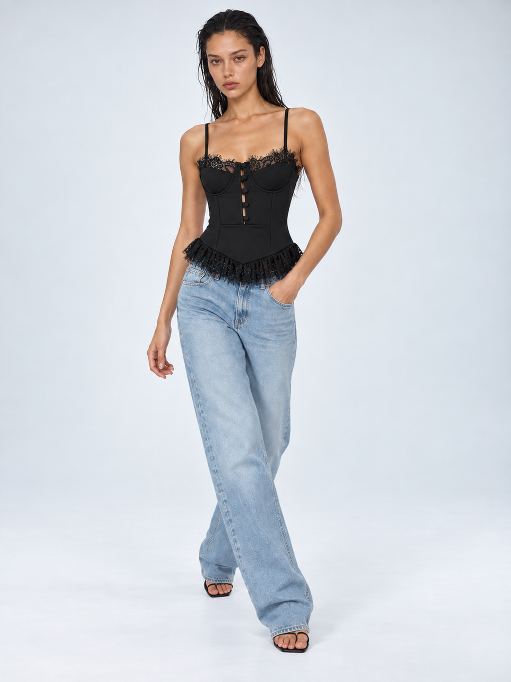 Elévaison Belle Tank Top in black, front view showing a fitted corset bodice, button detail and lace trim, styled with light blue jeans against a pale blue studio background.