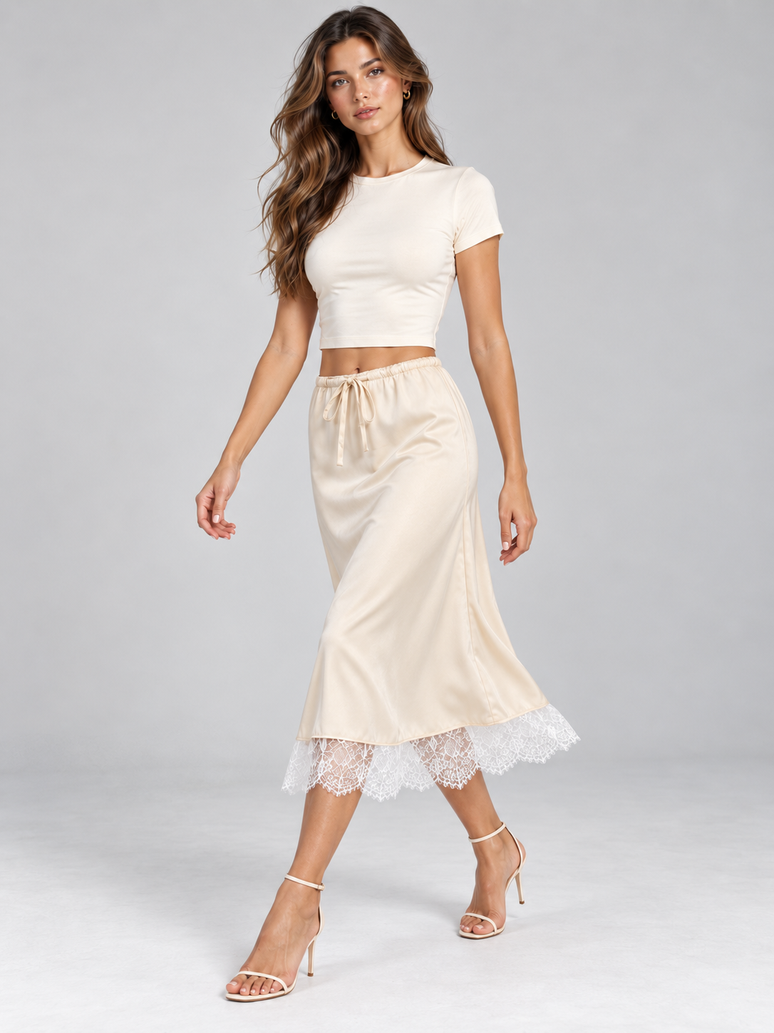 Elévaison Pearl Skirt in apricot, front walking view showing the drawstring waist and white lace-trimmed midi hem, styled with a white cropped T-shirt against a light gray studio background.