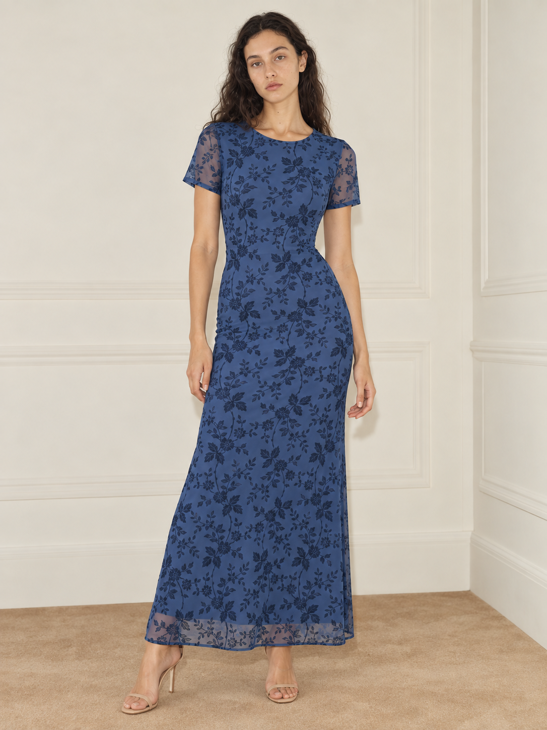 Elévaison Juliette Dress in blue, front view showing a fitted silhouette, short sheer sleeves and a dark floral overlay against a warm cream paneled studio background.