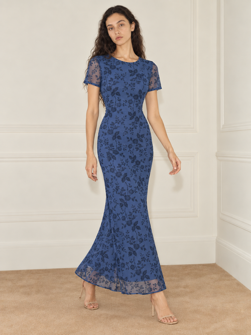 Elévaison Juliette Dress in blue, full-length front view showing a fitted silhouette, short sheer sleeves and a dark floral overlay against a warm cream paneled studio background.