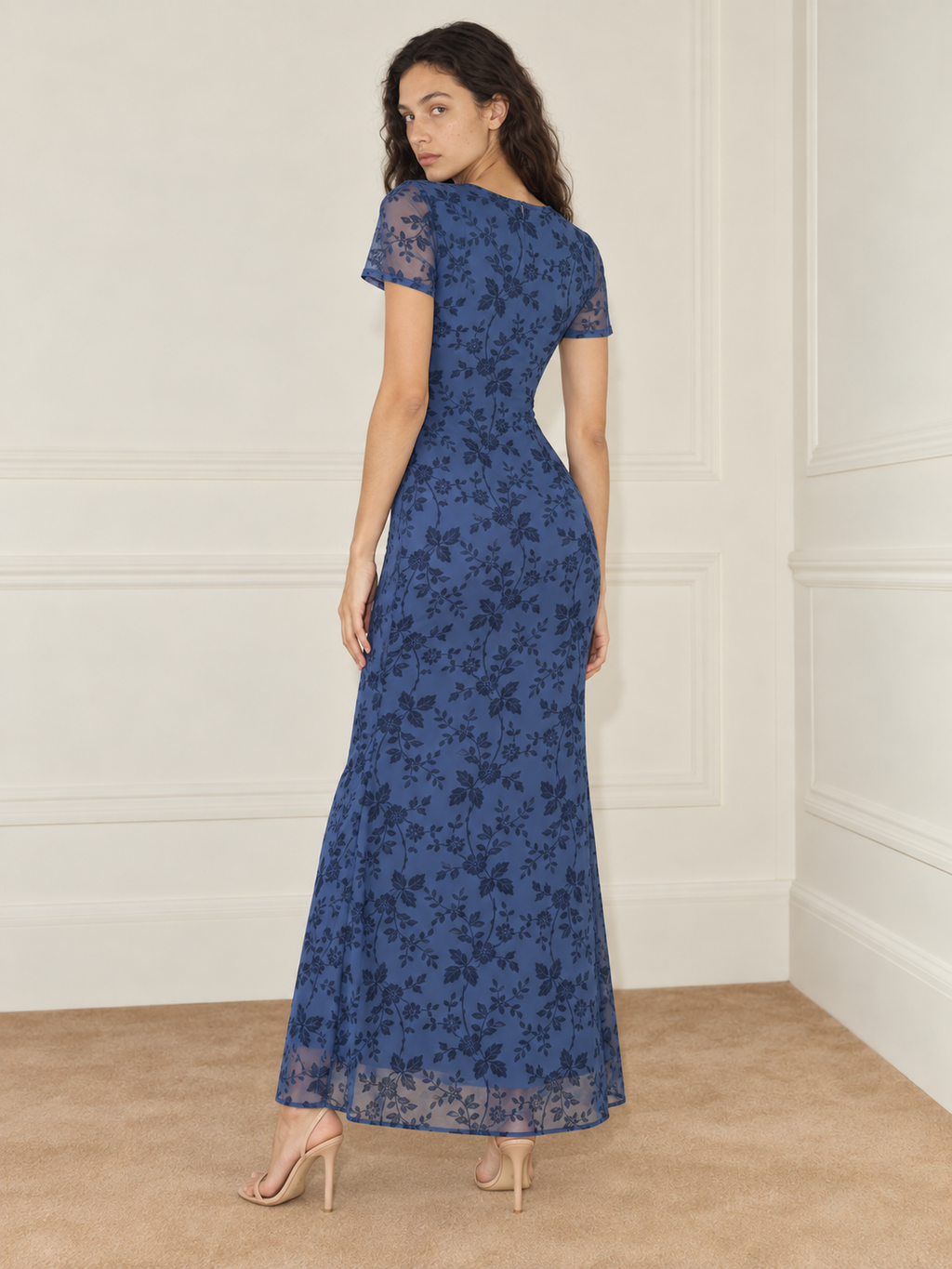 Elévaison Juliette Dress in blue, back view showing the fitted silhouette, short sheer sleeves and floral overlay against a warm cream paneled studio background.