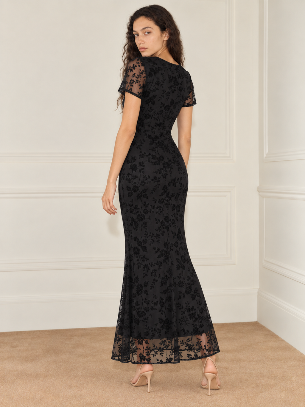 Elévaison Juliette Dress in black, back view showing the fitted silhouette, short sheer sleeves and sheer floral hem against a warm cream paneled studio background.