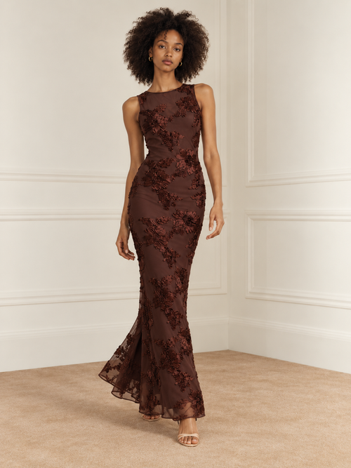 Elévaison Grace Dress in chocolate brown, full-length front walking view showing a sleeveless fitted silhouette and dimensional floral embroidery against a warm cream paneled studio background.