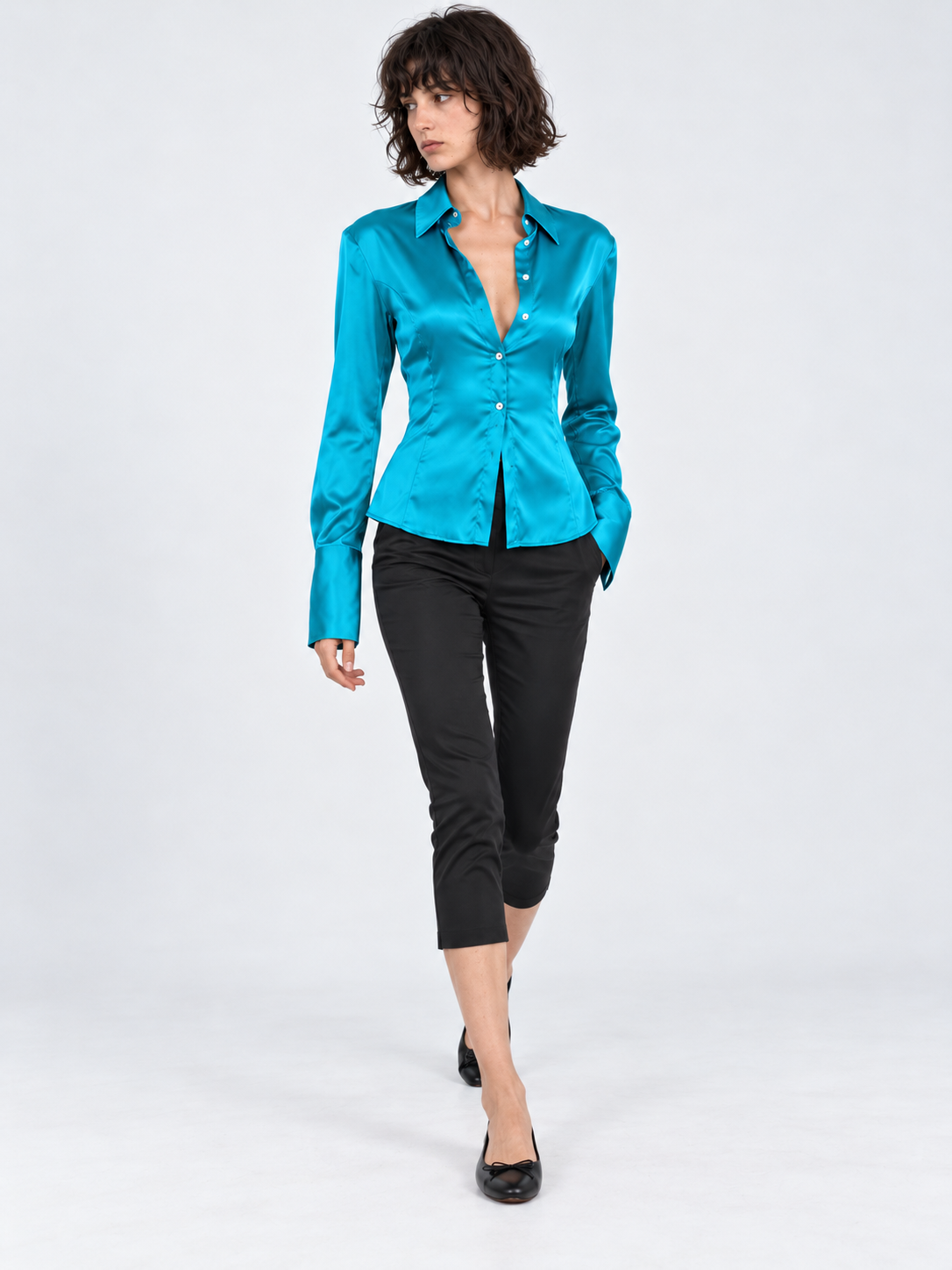 A model steps forward in the Elévaison Adrienne Shirt in Turquoise Blue, its satin finish catching the light against a gray backdrop.
