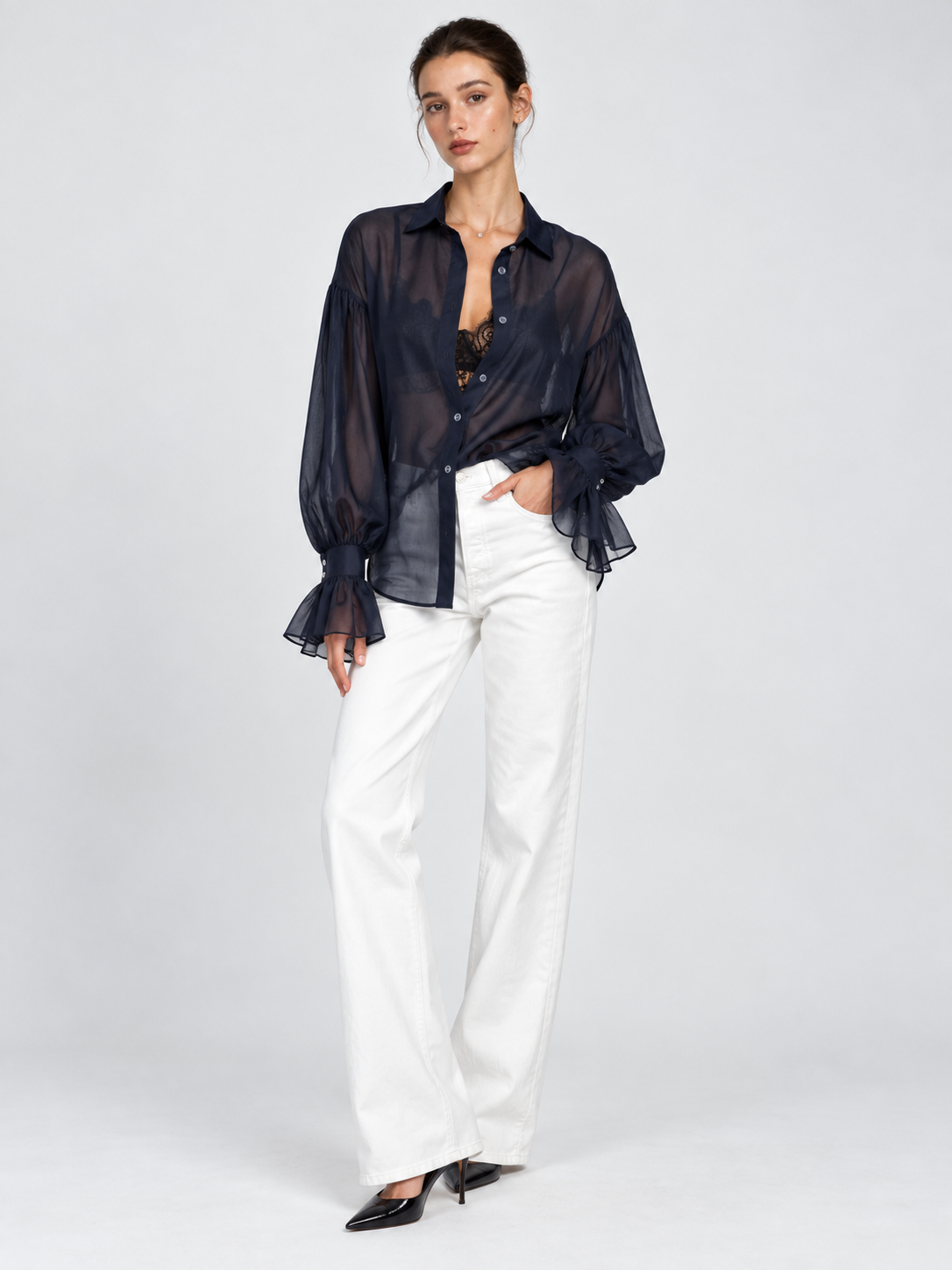 A model wears the sheer Elévaison Florence Blouse in Navy, with balloon sleeves and ruffled cuffs against a light gray backdrop.