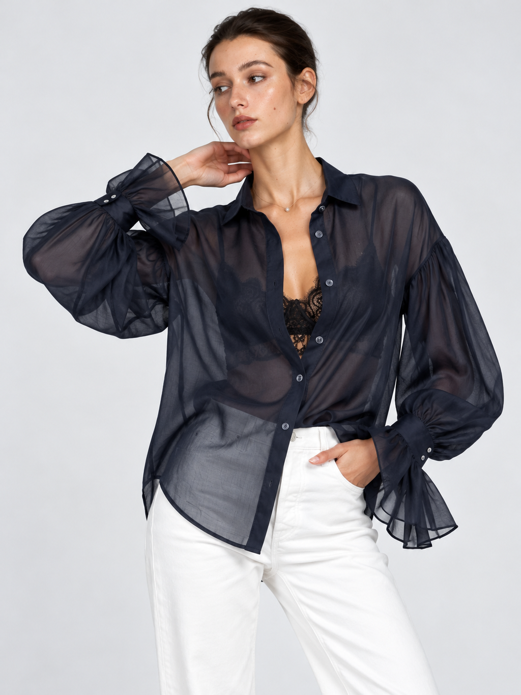 A model raises one arm in the Elévaison Florence Blouse in Navy, showing its full sleeve and ruffled cuff against a gray backdrop.