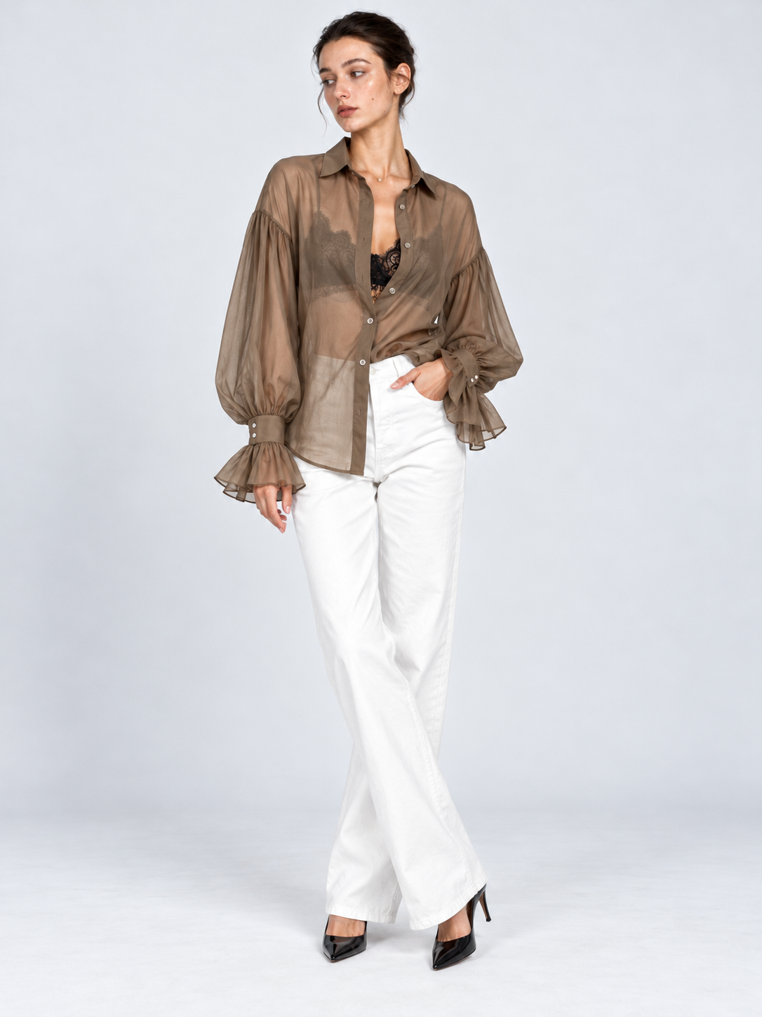 A model wears the Elévaison Florence Blouse in Khaki with white pants, showing its sheer front against a light gray studio backdrop.