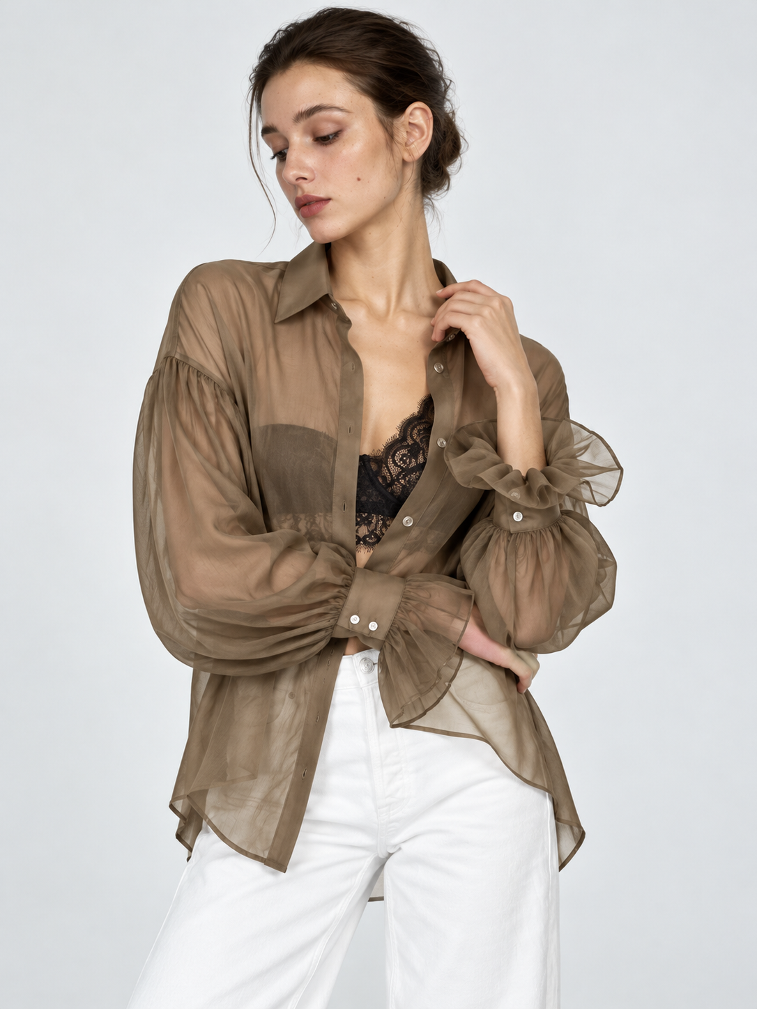 A model crosses her arms in the Elévaison Florence Blouse in Khaki, highlighting the ruffled cuffs against a light gray backdrop.