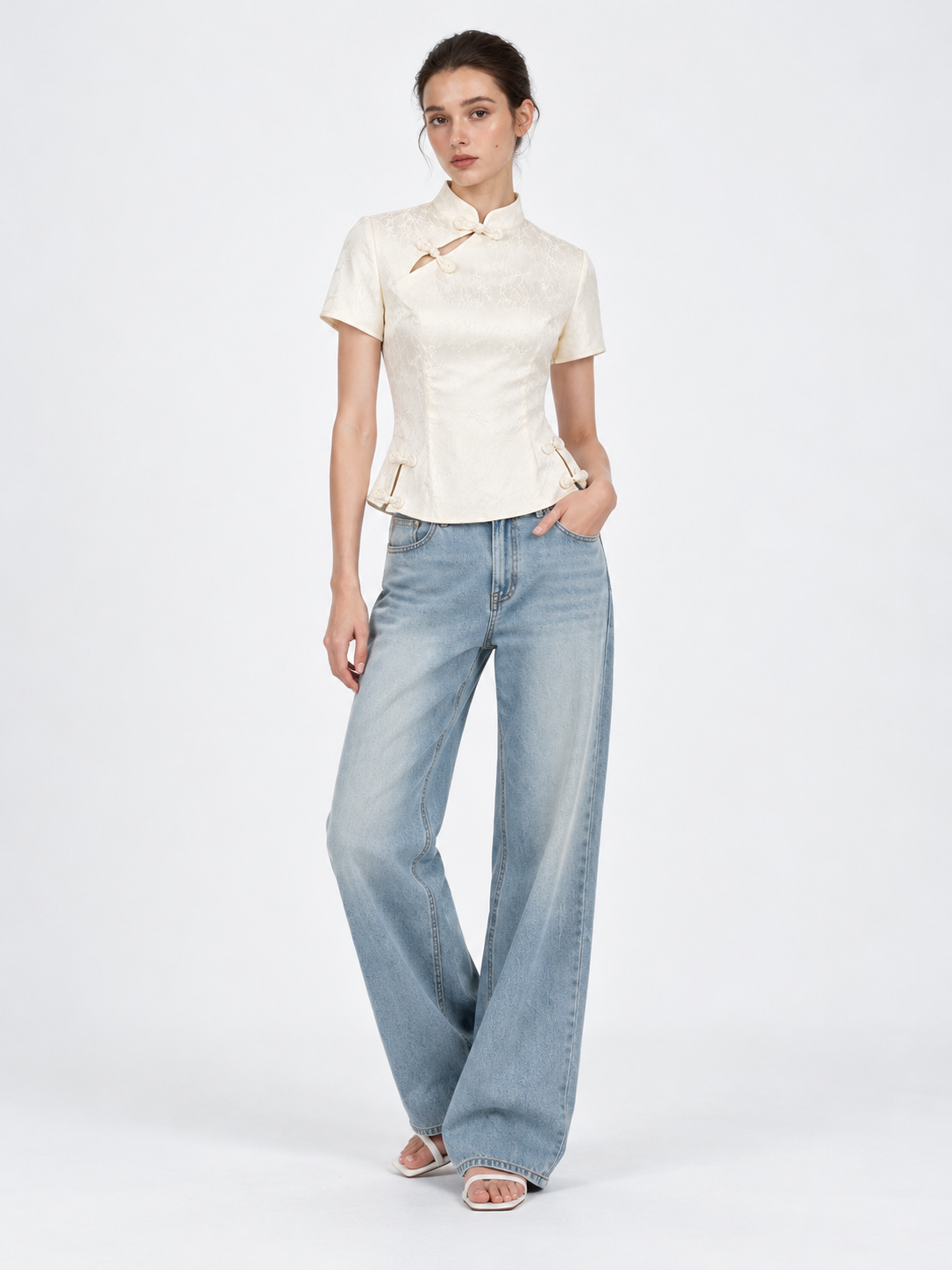 A model wears the Elévaison Beatrice Blouse in White with wide-leg jeans, showing its fitted waist against a light gray backdrop.