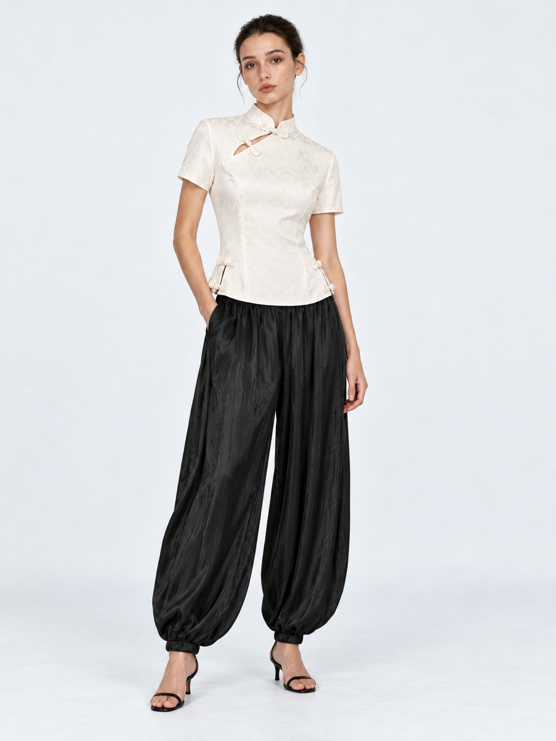 A model pairs the Elévaison Beatrice Blouse in White with black gathered pants against a light gray studio backdrop.