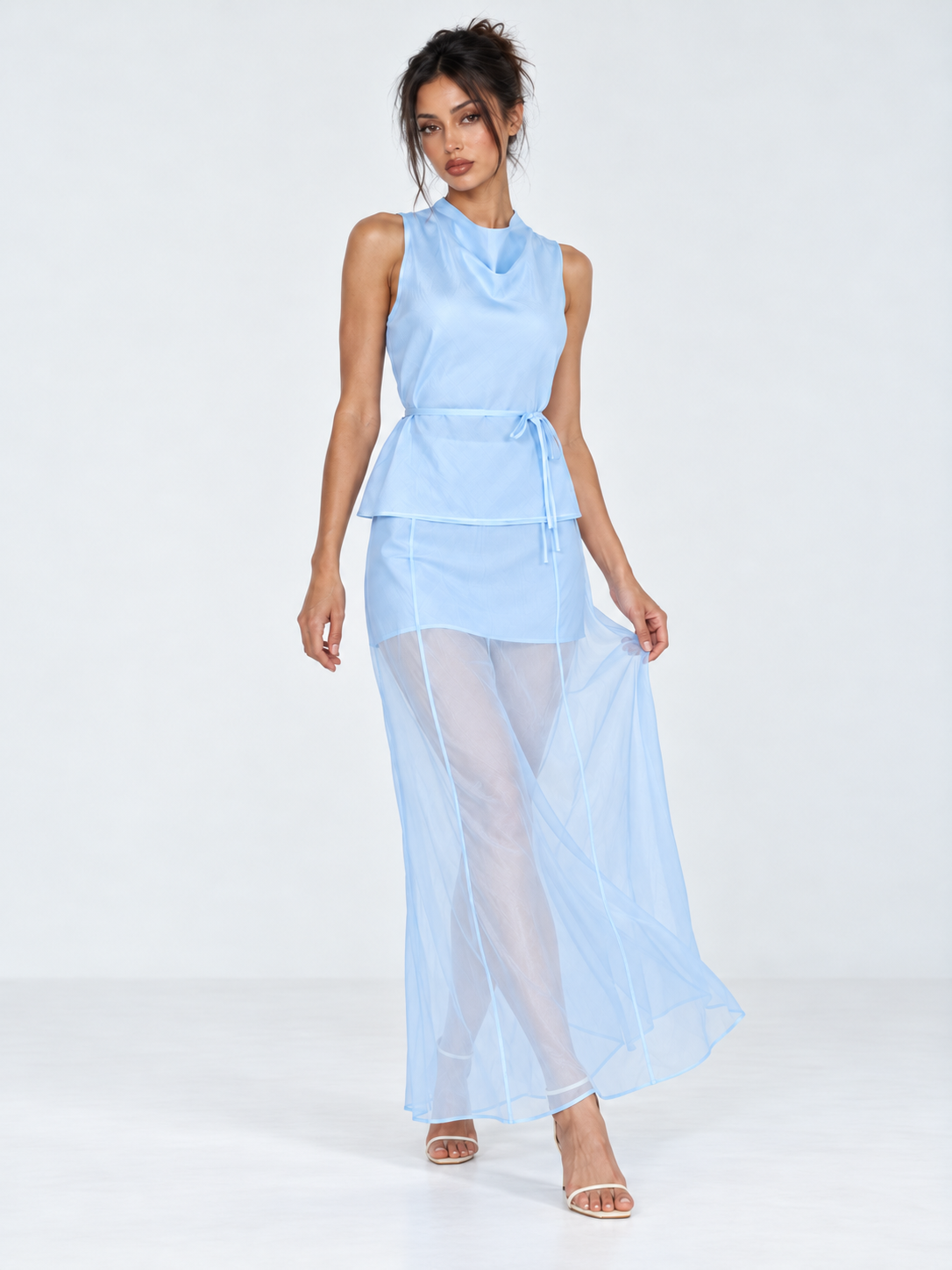 A model holds out the skirt of the Elévaison Alessia Two Piece in Blue, showing its sheer layers against a light gray backdrop.