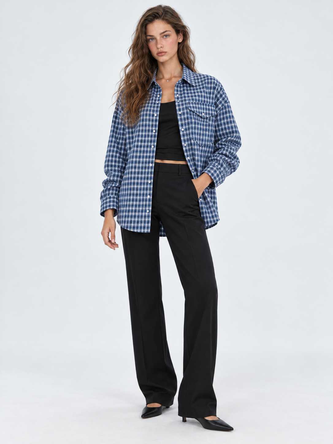 A model wears the Elévaison Audrey Cotton Shirt in Twilight Check open over a black top against a light gray studio backdrop.