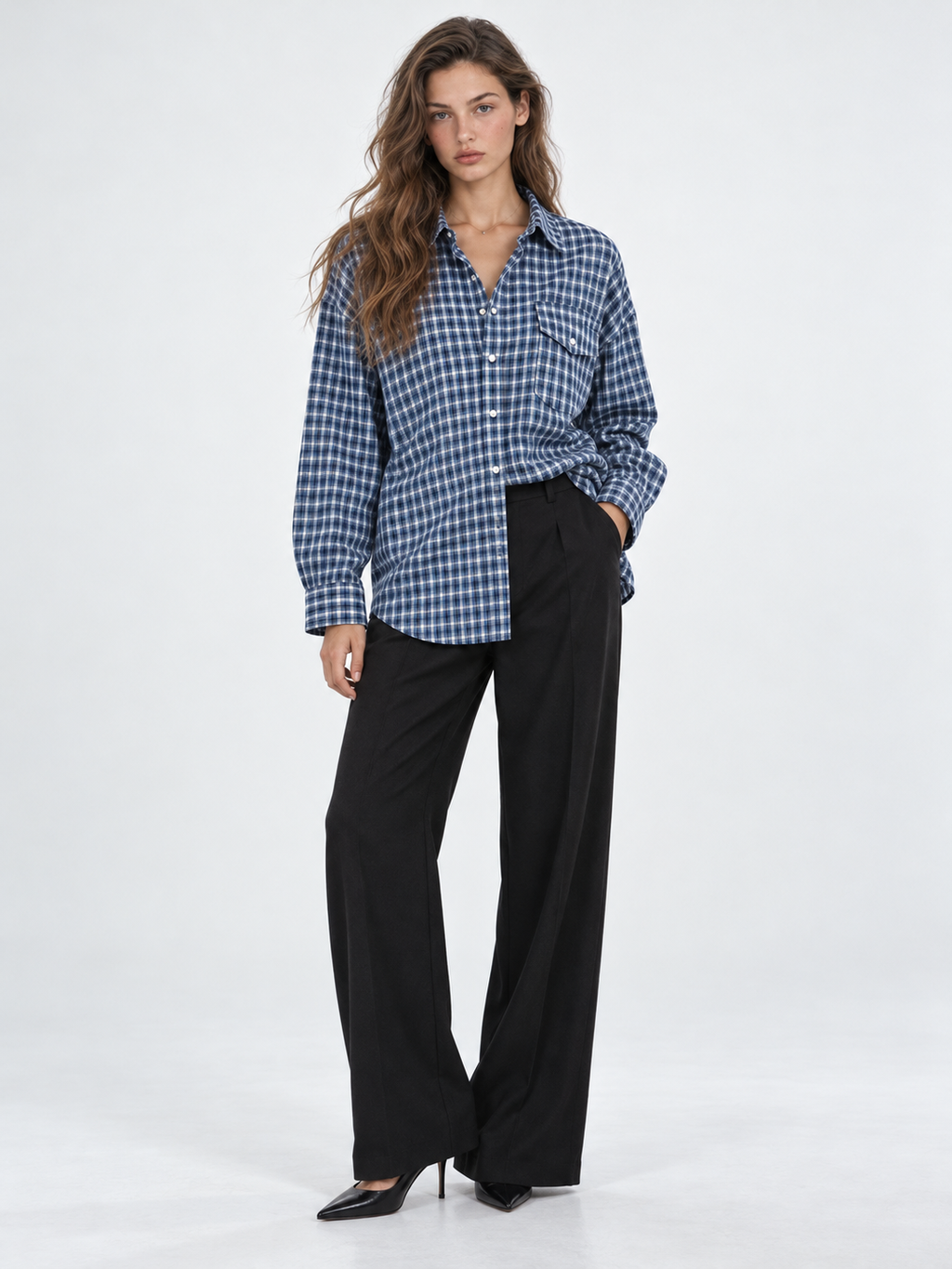 A model wears the Elévaison Audrey Cotton Shirt in Twilight Check partly tucked into black pants against a light gray backdrop.