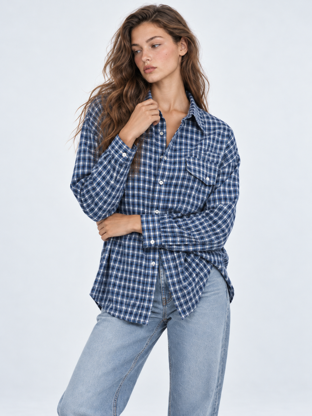 A model crosses one arm in the Elévaison Audrey Cotton Shirt in Twilight Check, showing its button front against a gray backdrop.