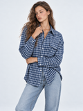 A model crosses one arm in the Elévaison Audrey Cotton Shirt in Twilight Check, showing its button front against a gray backdrop.
