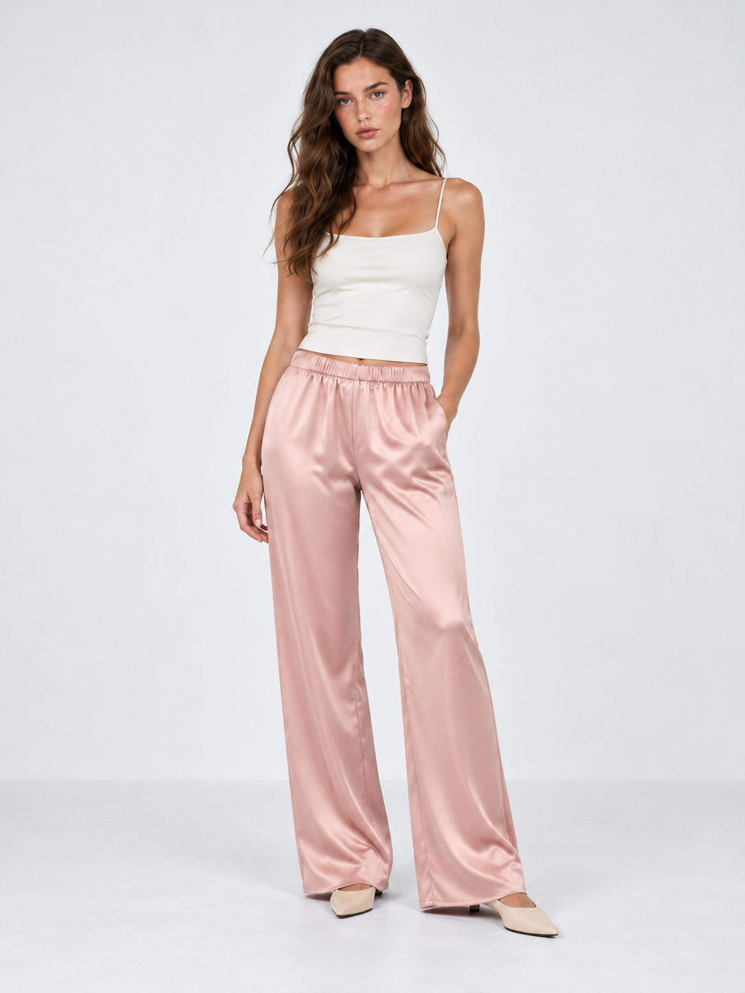 A model wears the Elévaison Helena Pants in Pink, with a gathered waistband and wide-leg silhouette against a light gray backdrop.