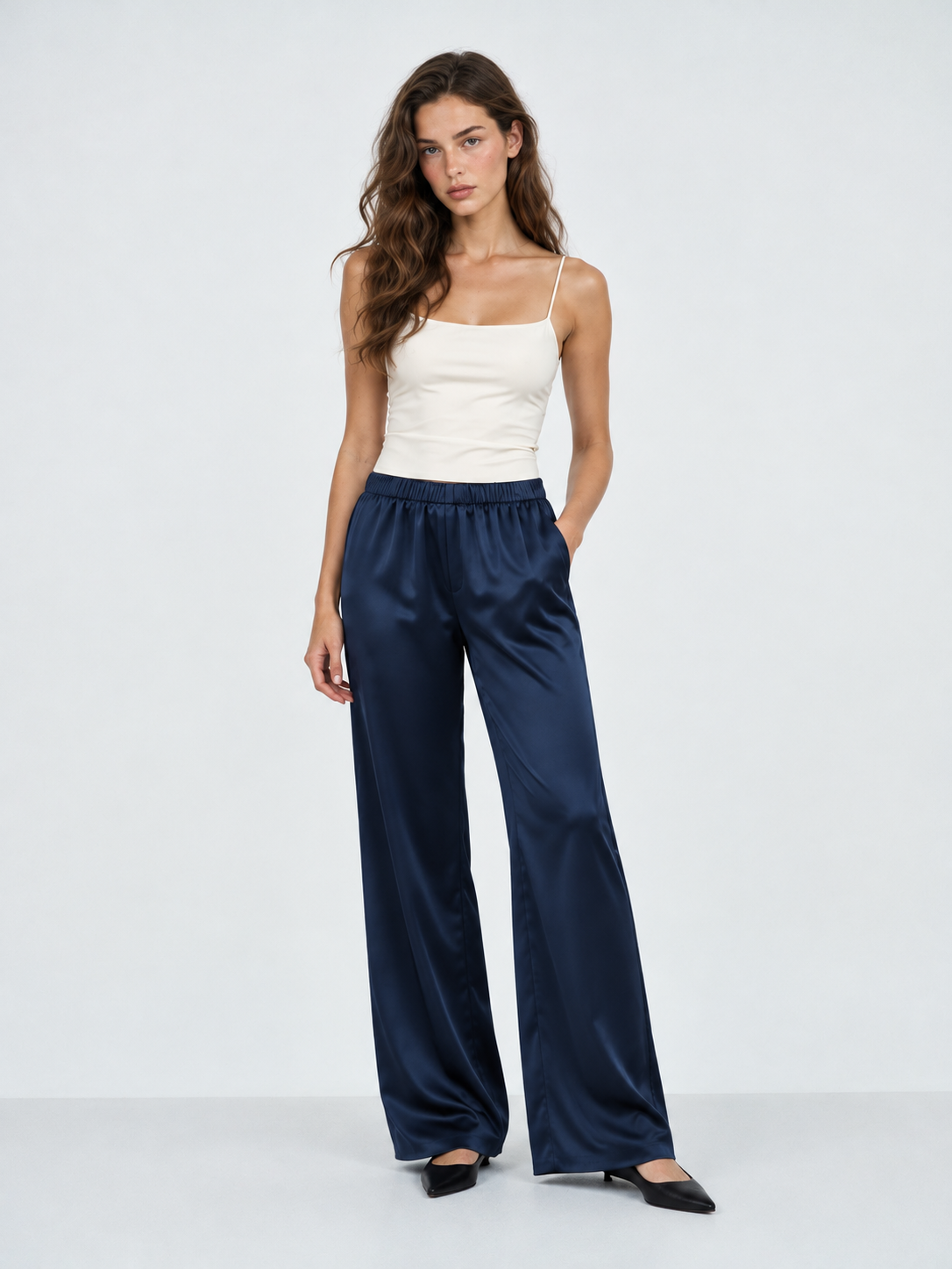 A model wears the Elévaison Helena Pants in Dark Blue, with one hand in a pocket and long wide legs against a light gray backdrop.