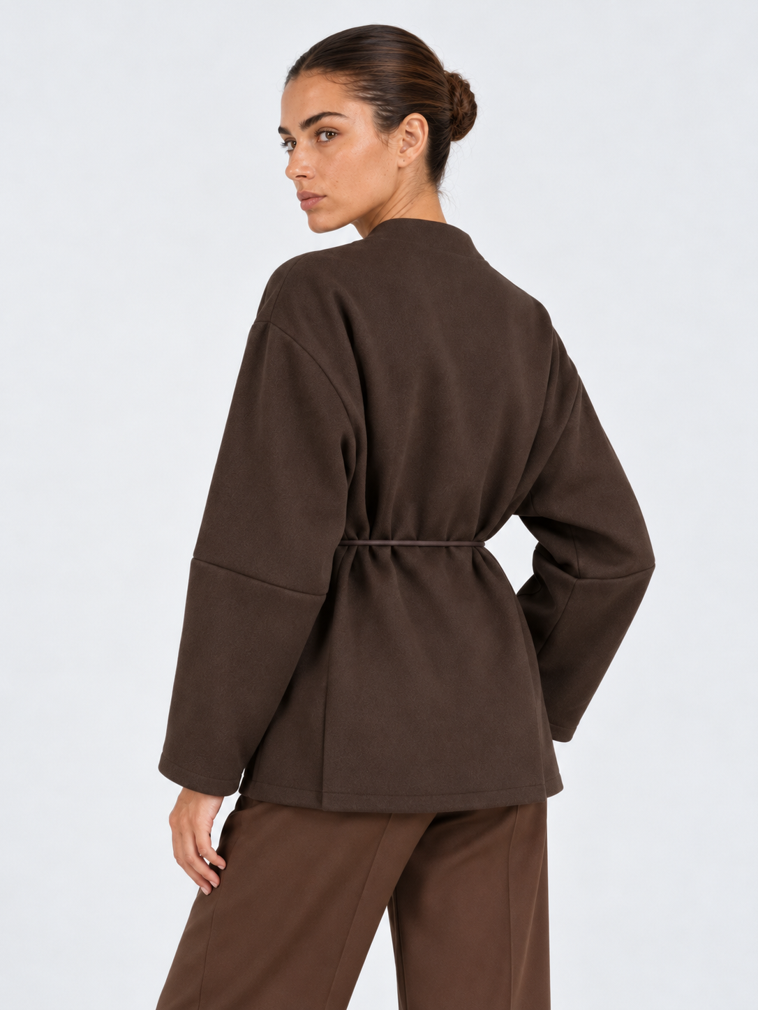 A closer rear view of the Elévaison Freya Jacket in Brown shows its cinched waist and broad sleeves against a light gray backdrop.