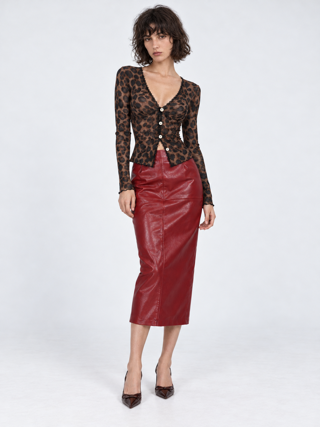 A model wears the Elévaison Bianca Skirt in Burgundy with a leopard cardigan, showing its midi length against a light gray backdrop.