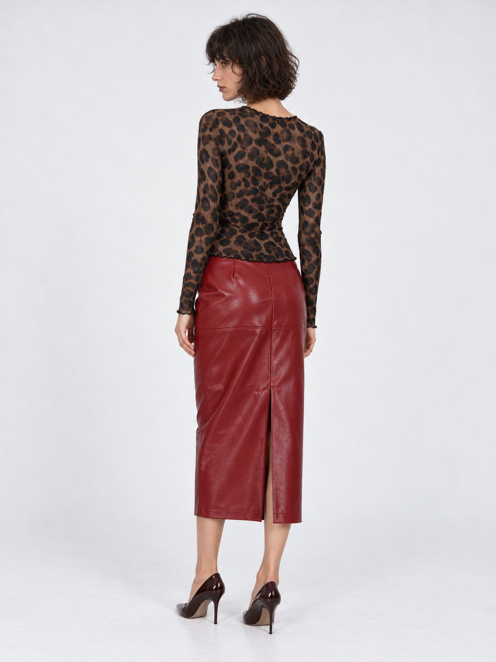 A model turns in the Elévaison Roxanne Cardigan in Amber Leopard, showing its fitted back and long sleeves against a gray backdrop.