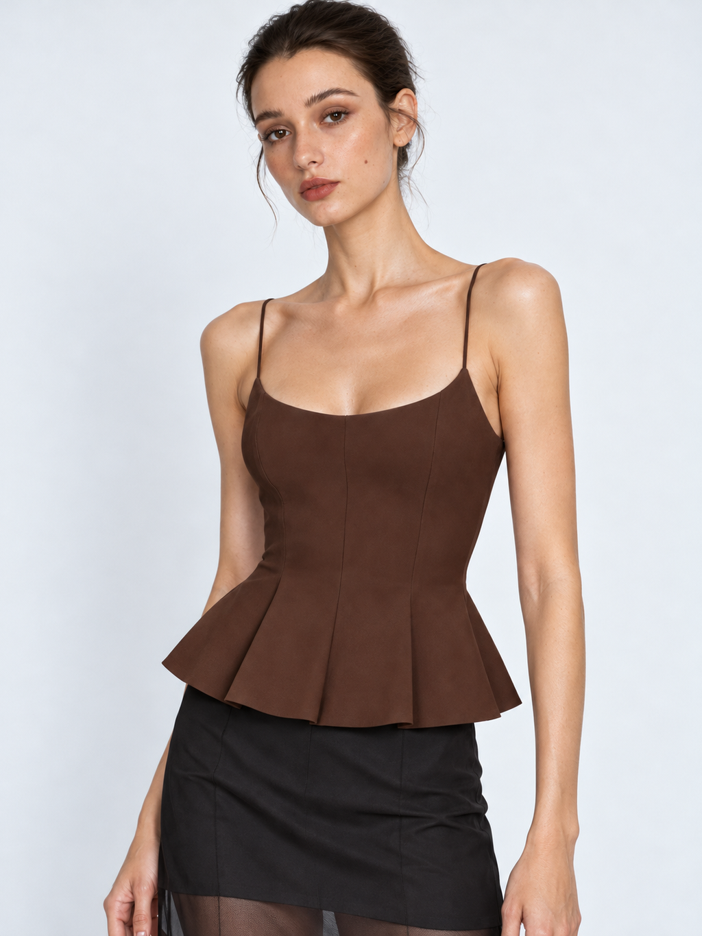 A closer view of the Elévaison Celia Camisole in Brown shows its fitted waist and pleated peplum against a light gray backdrop.