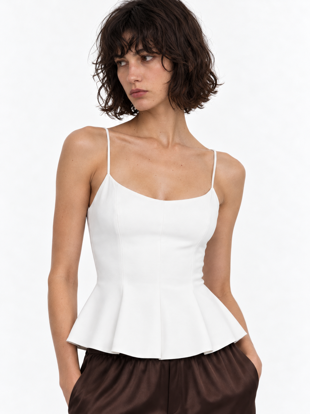 A closer view of the Elévaison Celia Camisole in White shows its thin straps and flared peplum hem against a light gray backdrop.