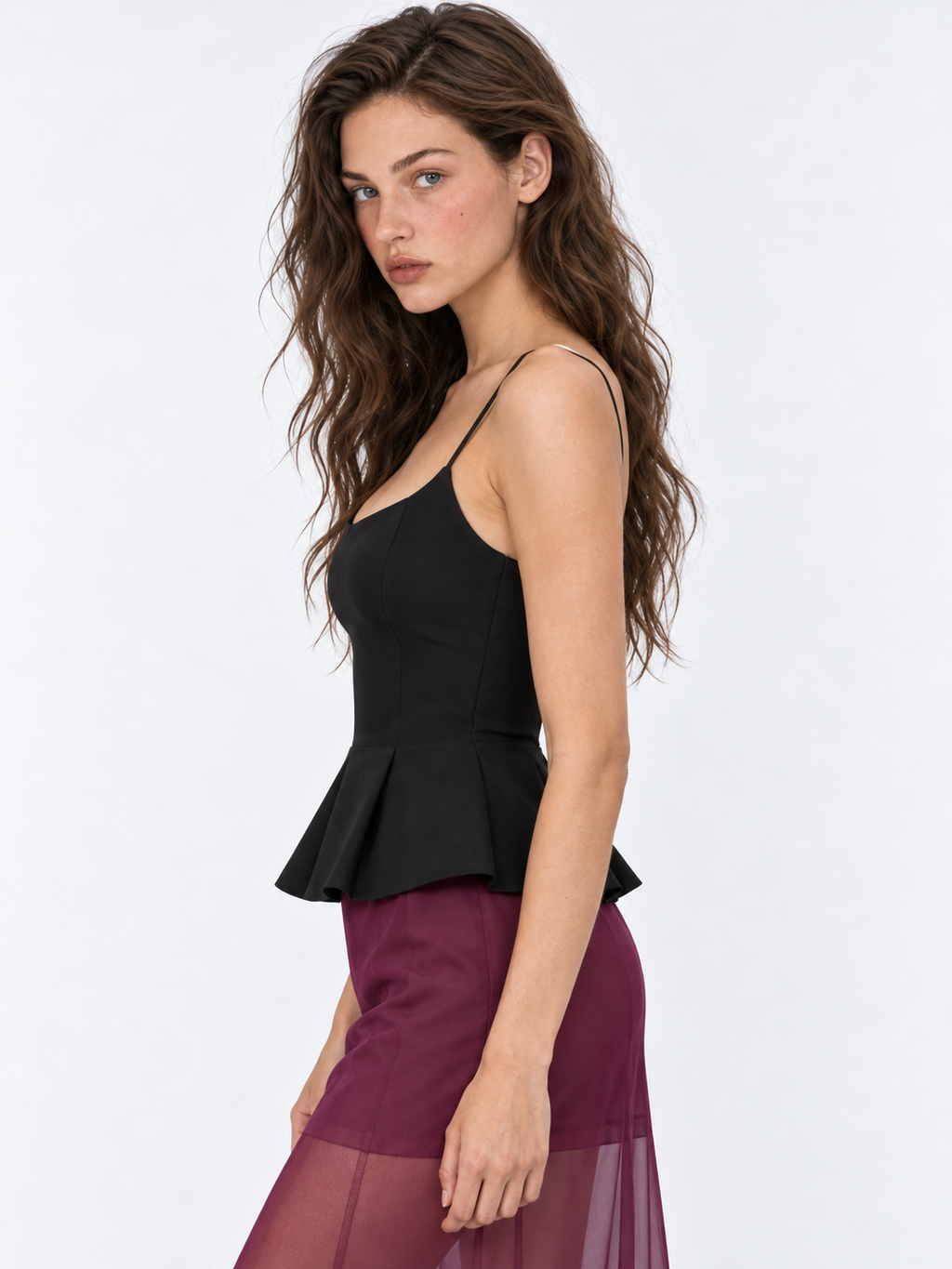A side view of the Elévaison Celia Camisole in Black shows its shaped waist and pleated peplum against a light gray studio backdrop.
