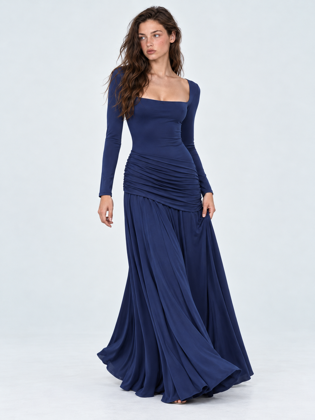 A model holds out the skirt of the Elévaison Arabella Dress in Dark Blue, showing its flowing folds against a light gray backdrop.
