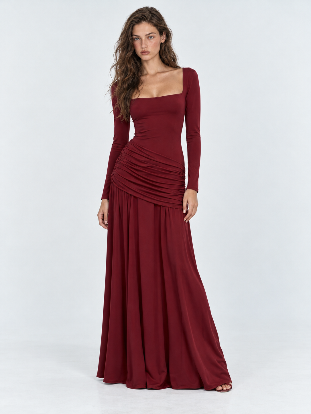 A model wears the Elévaison Arabella Dress in Burgundy, showing long sleeves and a gathered hip panel against a light gray backdrop.