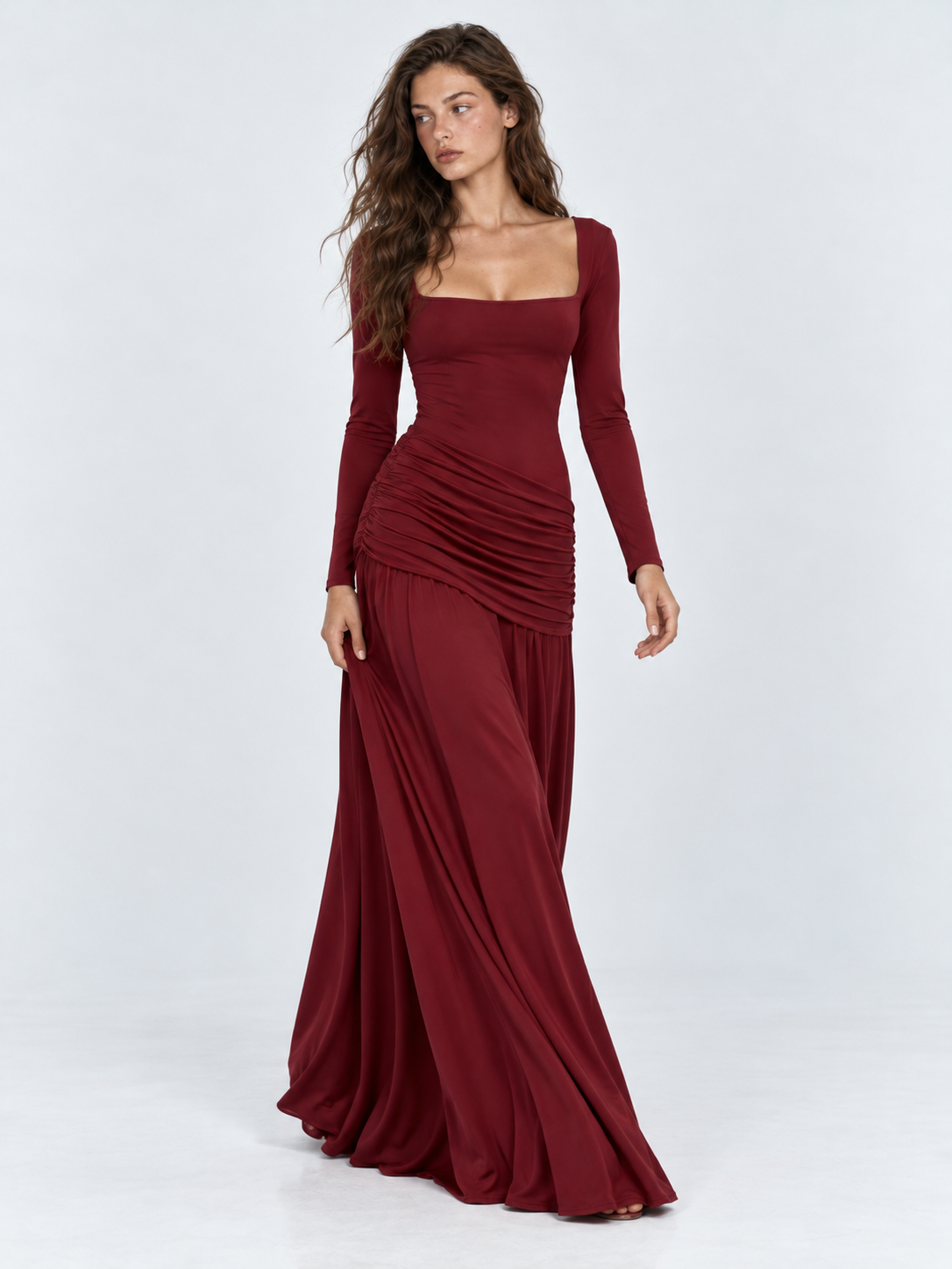 A model steps forward in the Elévaison Arabella Dress in Burgundy, showing the drape of its maxi skirt against a light gray backdrop.