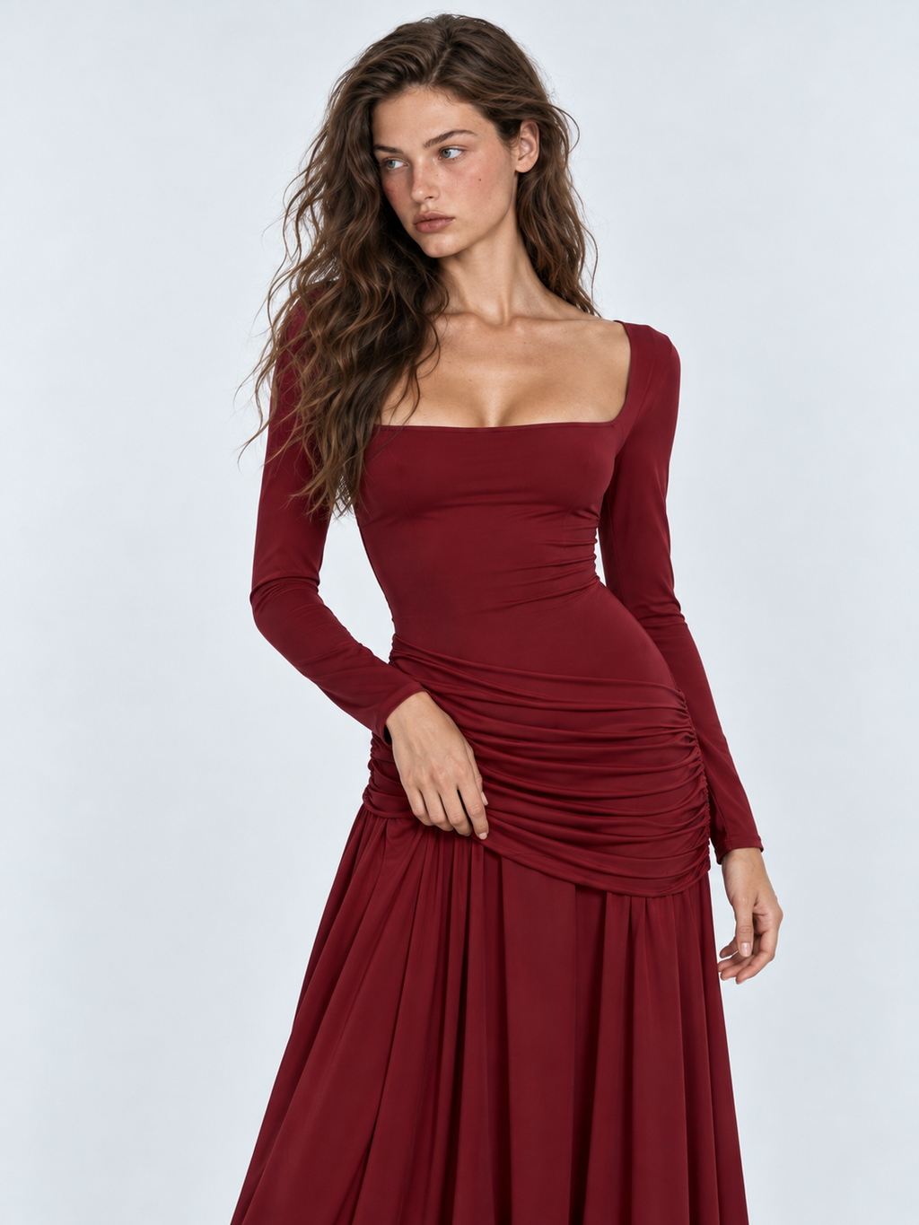A closer view of the Elévaison Arabella Dress in Burgundy shows its square neckline and gathered hip panel against a gray backdrop.