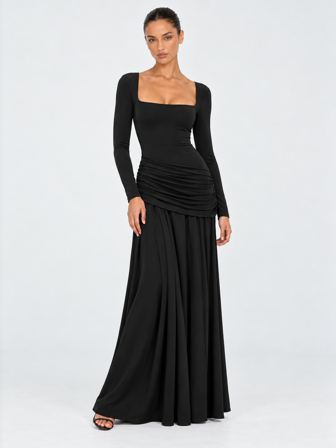 A model wears the Elévaison Arabella Dress in Black, with a square neckline and full-length skirt against a light gray backdrop.