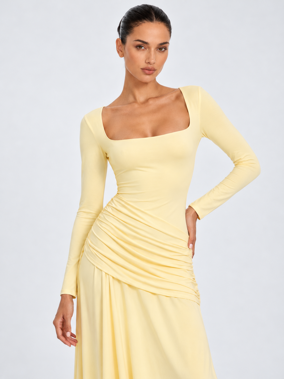 A closer view of the Elévaison Arabella Dress in Light Yellow shows its square neckline and ruched hips against a gray backdrop.