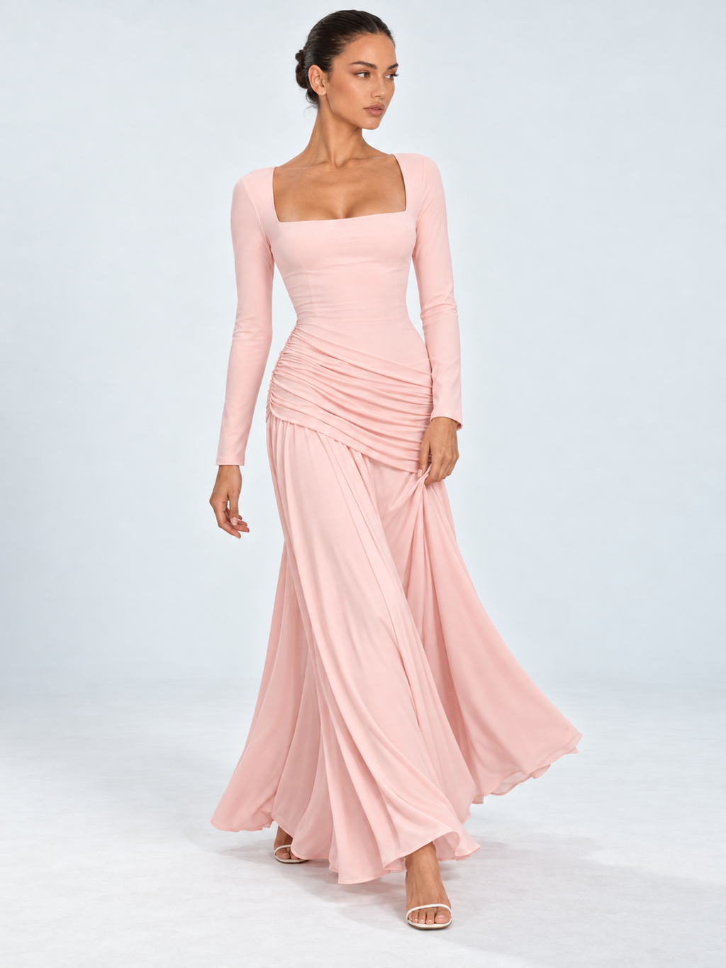 A model steps forward in the Elévaison Arabella Dress in Pink, its full-length skirt sweeping outward against a light gray backdrop.