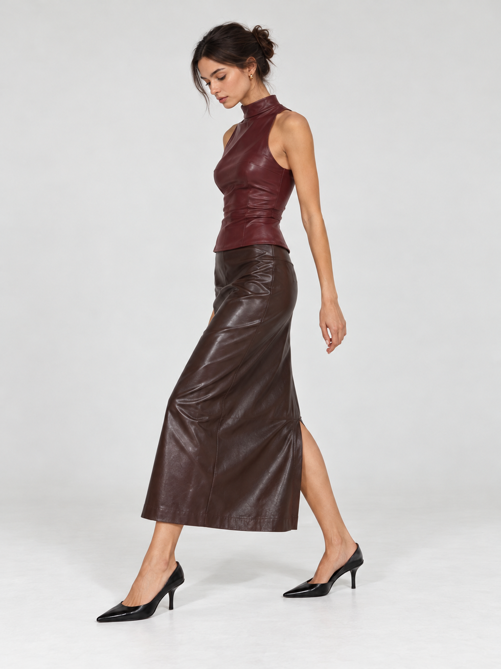 A model walks in the Elévaison Carmen Top in Burgundy, showing its sleeveless cut and glossy surface against a light gray backdrop.
